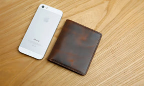 Carteira de couro marrom ao lado de um iPhone em fundo de madeira