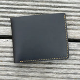 Carteira de couro preto com costura amarela, elegante e compacta.