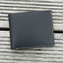 Carteira de couro preto com costura amarela, elegante e compacta.