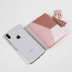 carteira feminina na cor rosa sendo exibida ao lado de um iphone para demonstração de seu tamanho compacto.