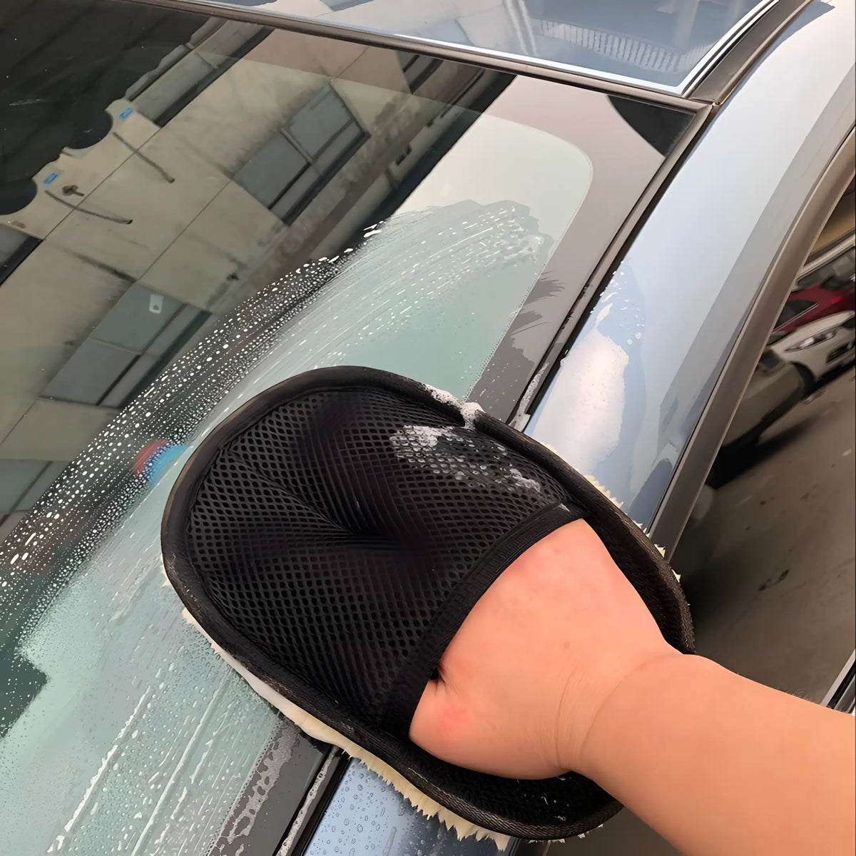 Uma pessoa usando a luva de limpeza para lavar o para-brisa do carro.