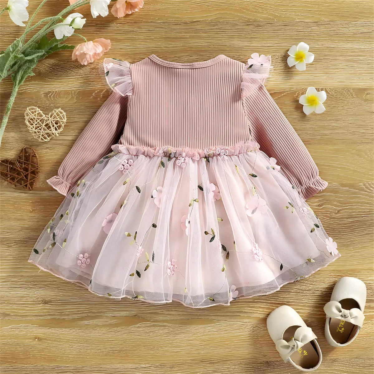 vestido infantil para menina rosa floral em exibição ao lado de um sapato e flores.